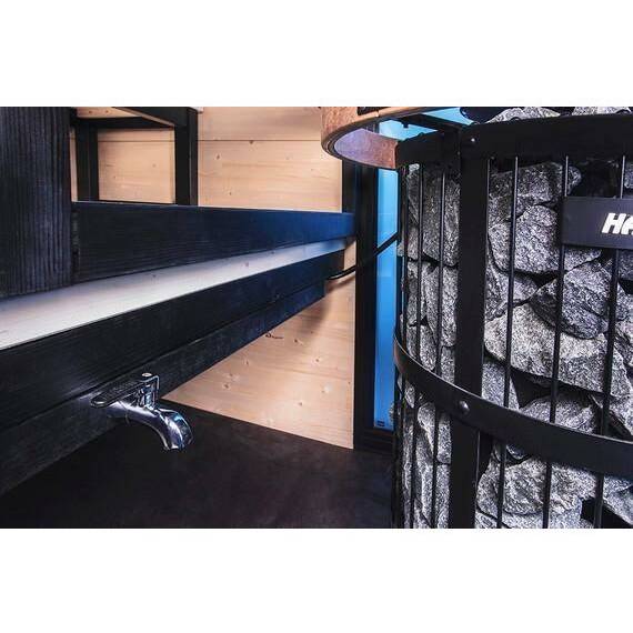 Harvia WP250LD Sauna Water Heater for Legend Stoves, 25 Liter, chrome faucet mounted beneath a black topped bench with the heater cage nearby