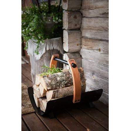 Harvia Legend Firewood Basket SASPO102 filled with birch logs on a rustic wood porch with potted greenery and log cabin wall