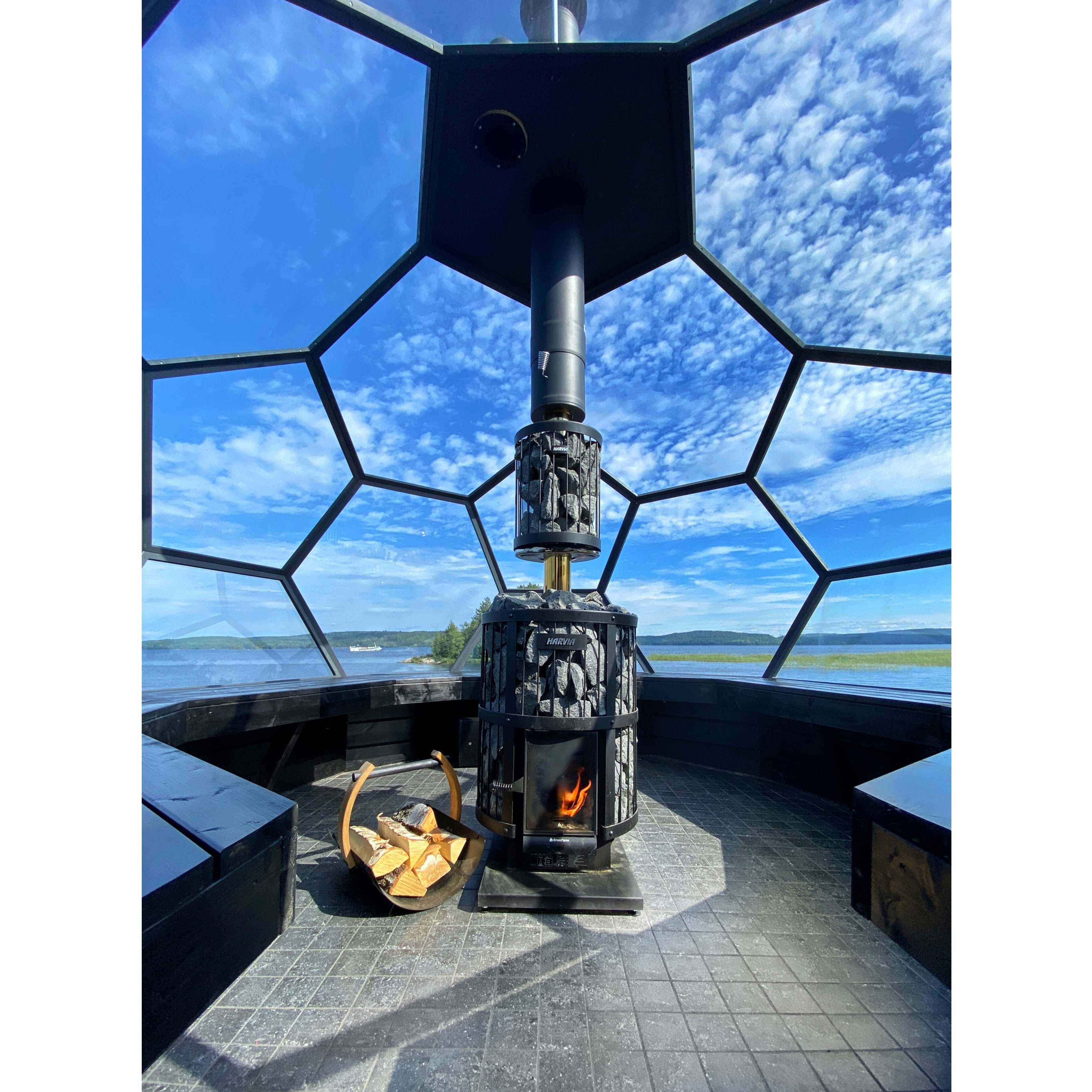 Harvia Legend 240 GreenFlame 21kW Wood-Burning Sauna Stove burning inside a glass domed sauna with lake and sky views and a log basket.