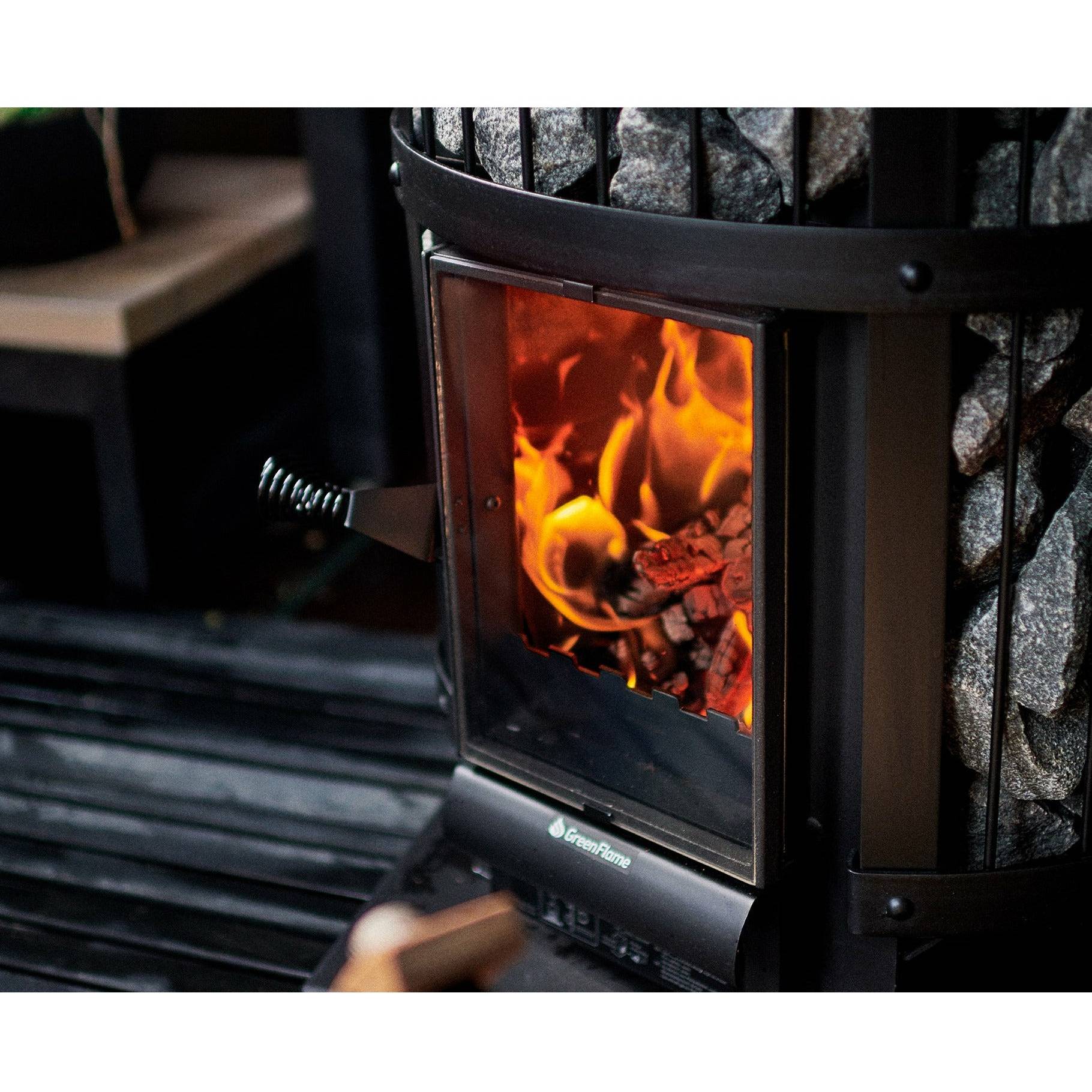 Harvia Legend 240 GreenFlame 21kW Wood-Burning Sauna Stove, close up of the glass door with burning logs and a hand loading a wood log.