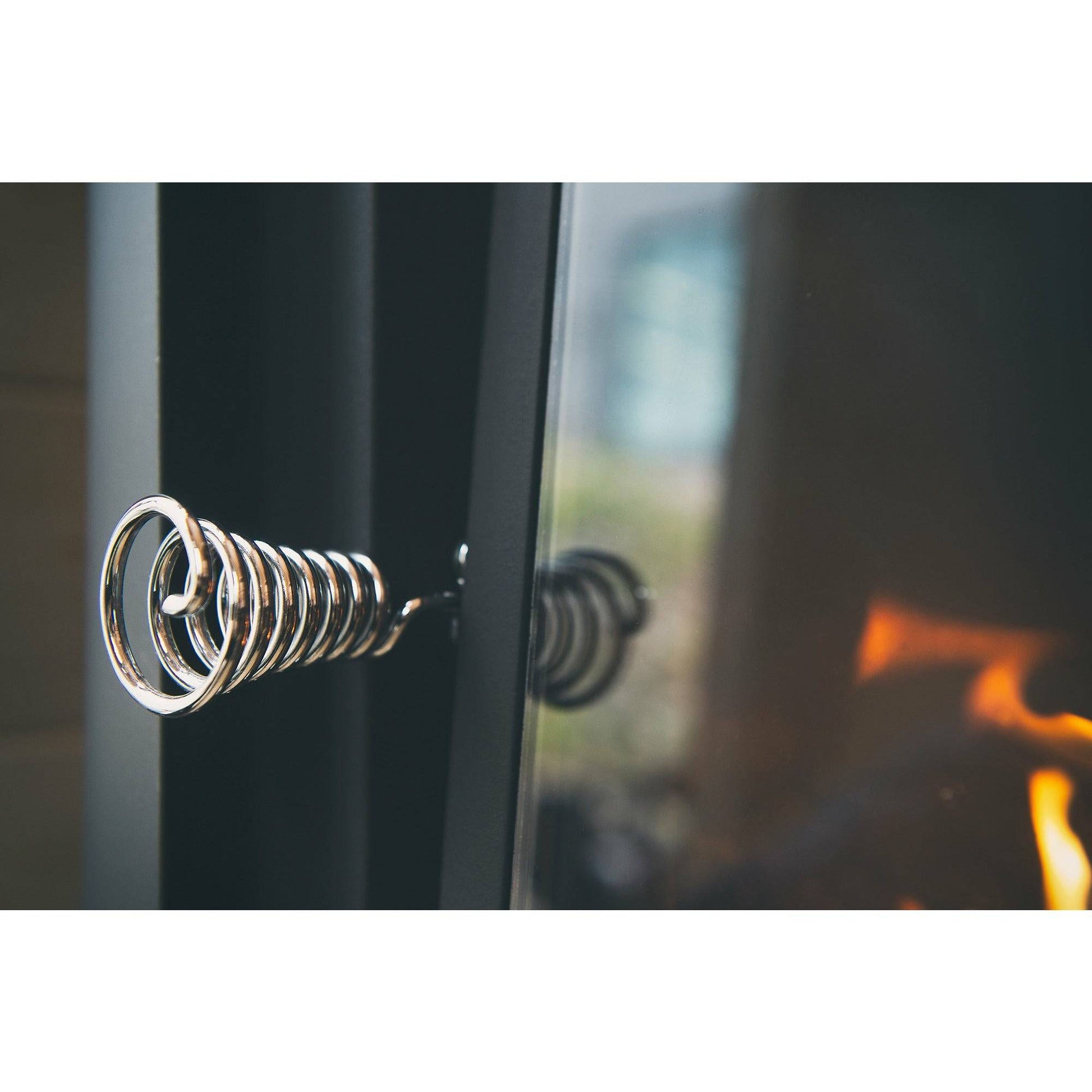 Harvia Pro 20 LS Wood-Burning Sauna Stove with Water Tank, close-up of the coiled chrome door handle with the fire glowing behind the glass.
