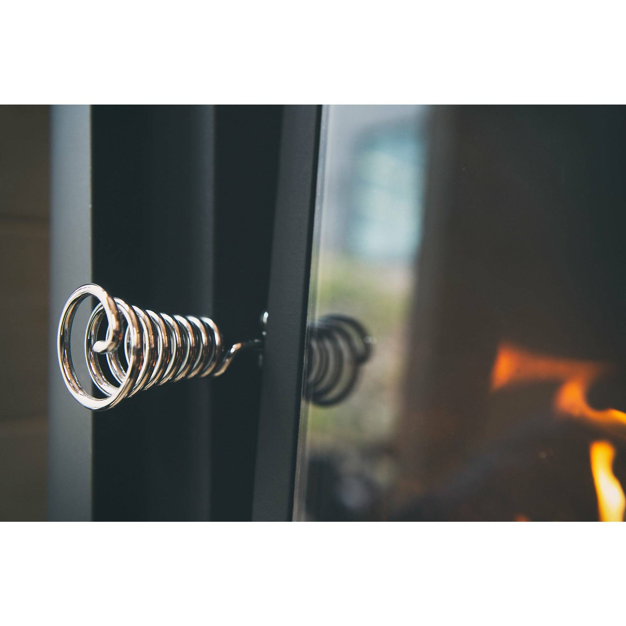 Harvia Pro 20 LS Wood-Burning Sauna Stove with Water Tank, close-up of the coiled chrome door handle with the fire glowing behind the glass.