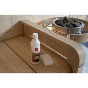 Harvia Sauna Heater Cleanser 500ml bottle with cleaning sponge on wooden bench beside heater and stones