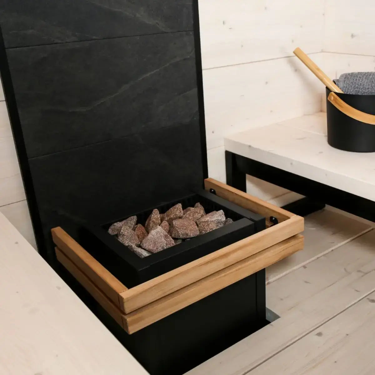 Harvia Virta HL110 10.5kW Ultimate Electric Sauna Heater Kit, installed in a sauna beside a bench with a wooden bucket and ladle.
