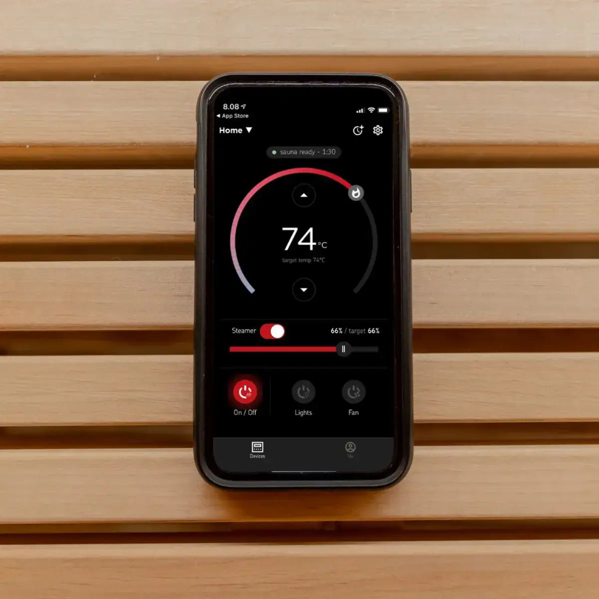 Harvia Virta HL80 8kW Ultimate Electric Sauna Heater Kit, smartphone app showing temperature and steamer controls resting on a wood bench.