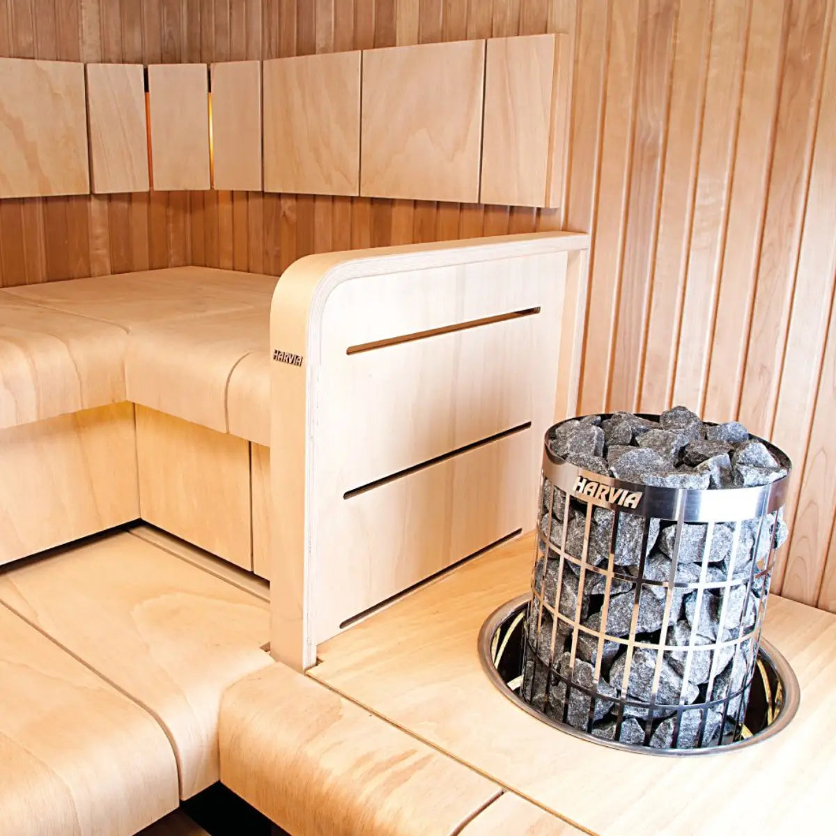 Harvia Cilindro PC90 9kW Electric Sauna Heater with Built-In Controls, installed beside a wood bench corner in a sauna with wood paneled walls.
