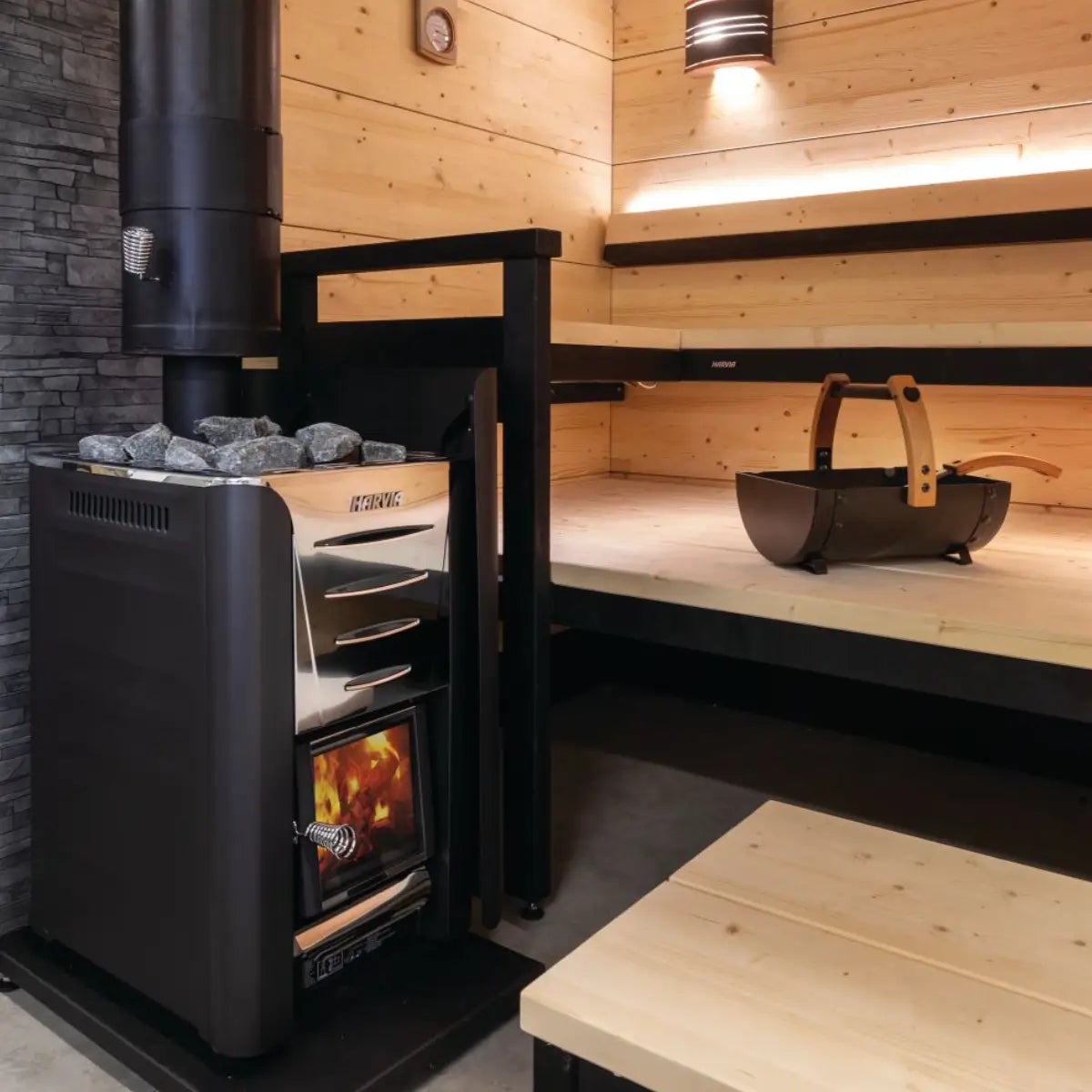 Harvia Pro 20 24kW Wood-Burning Sauna Stove installed in a wood-paneled sauna with chimney pipe, wood carrier, and bench.