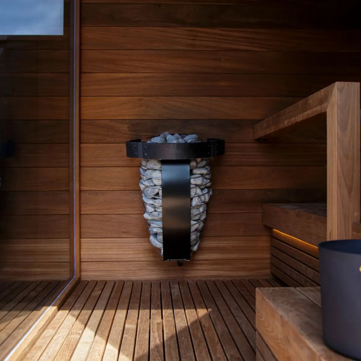 Harvia Spirit HSP3M Sauna Safety Railing, black guard rail installed around a stone clad heater in a wood paneled sauna interior.