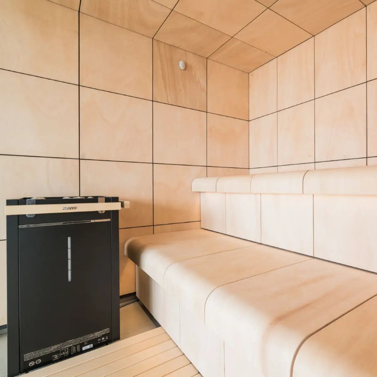 Harvia Virta Combi HL80SA 8kW Electric Sauna Heater and Steamer, mounted in a plywood-paneled sauna next to contoured light wood benches