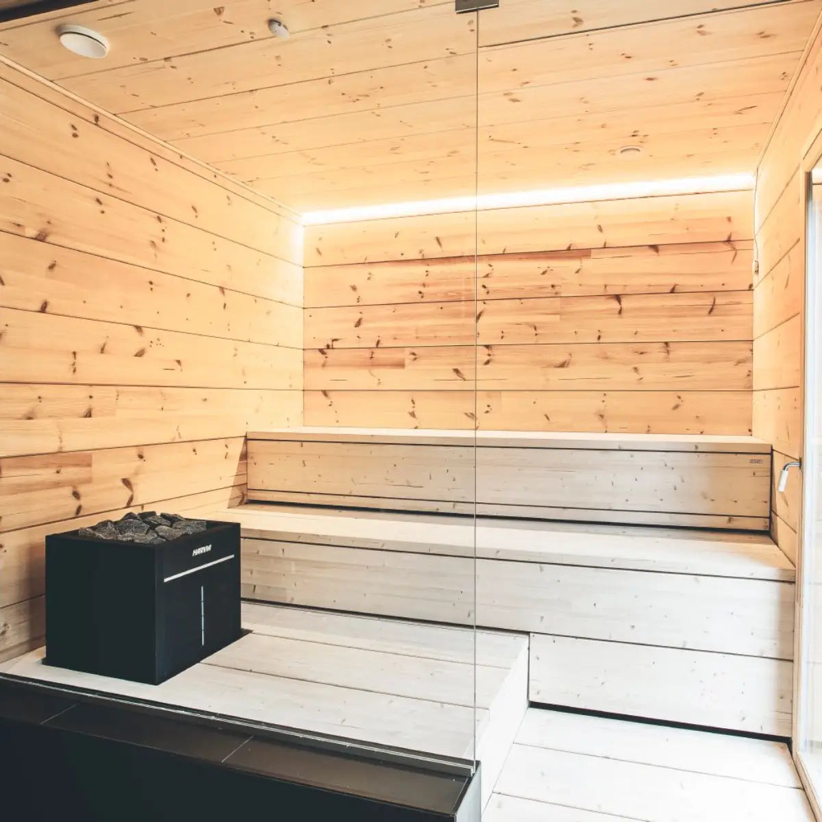 Harvia Virta Combi HL90SA 9kW Electric Sauna Heater with Steamer, installed in a modern wood sauna with tiered benches and LED lighting.