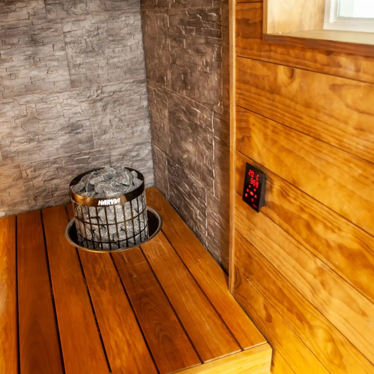 Harvia Xenio CX170-U3-15-XW Wi-Fi Sauna Control Unit installed on a sauna interior wall with a stone heater and window in view.
