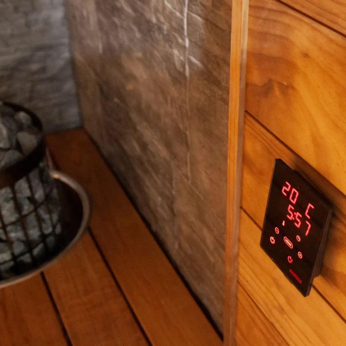 Harvia Xenio CX30C-U3-XW Wi-Fi Sauna Control Unit, wall mounted control panel beside the heater with stones inside a wood sauna