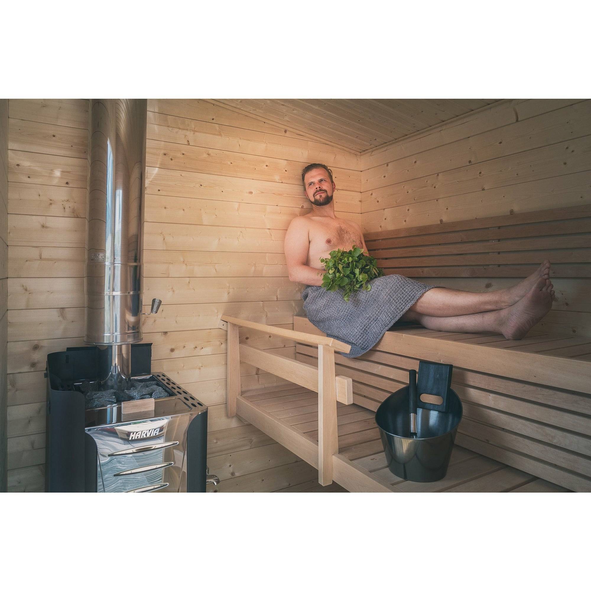 Harvia Pro 36 Wood-Burning Sauna Stove in a wood sauna interior with a man relaxing on the bench holding a leafy whisk.
