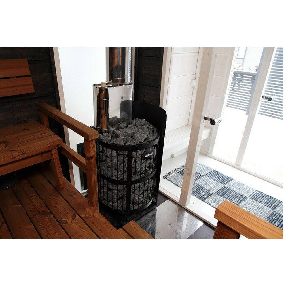 Harvia Legend WL200 Protective Wall Sheath, stove installed in a wood paneled sauna with chimney pipe, bench, and glass door to a snowy deck.