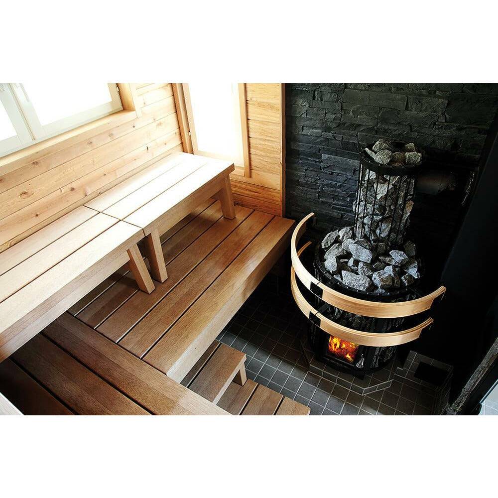 Harvia Legend WL300 Smoke Pipe Cover, installed on a wood burning stove in a sauna with wood benches, black stone wall, and glowing fire visible below