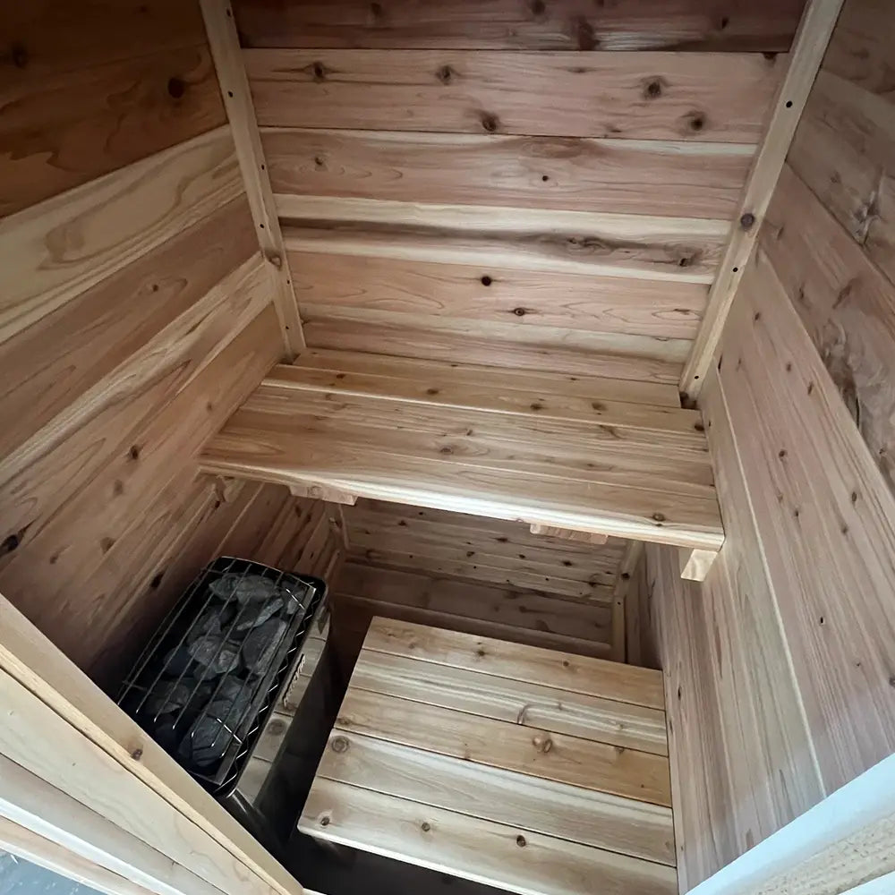 Interior of The Sweat Box one-person cedar sauna showing compact bench, cedar wall paneling, and sauna heater.