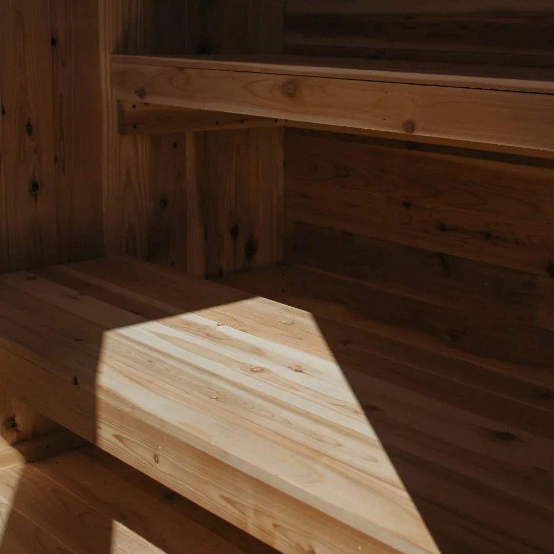 Interior corner of The Summit cedar sauna showing cedar walls, bench cross-section, and sunlight streaming in from the side window.