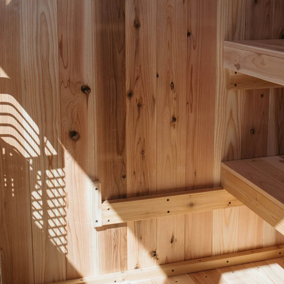 Close-up of The Summit cedar sauna exterior showing the slanted black-trim metal roof, round vent, cedar peg rack, and front door detail.