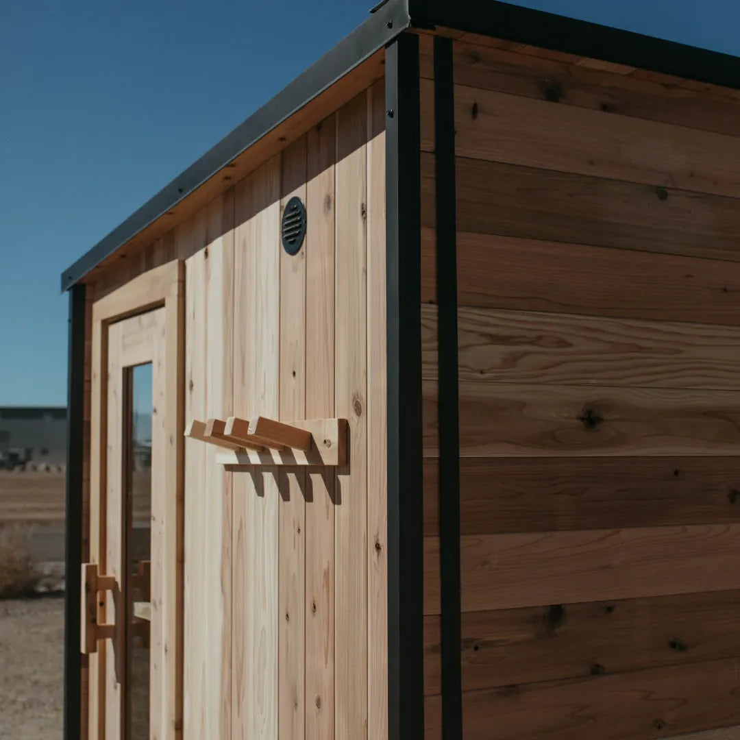 Close-up of The Summit cedar sauna corner detail showing the slanted black-trim roof, side picture window, and contrasting cedar siding.