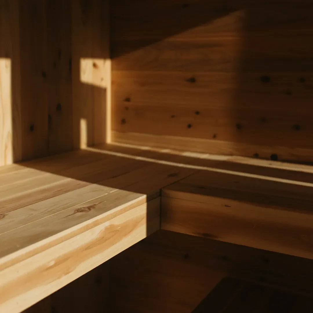 Interior view of The Sweat Cabin Deluxe sauna showing the L-shaped two-tier cedar bench layout with natural light streaming in.