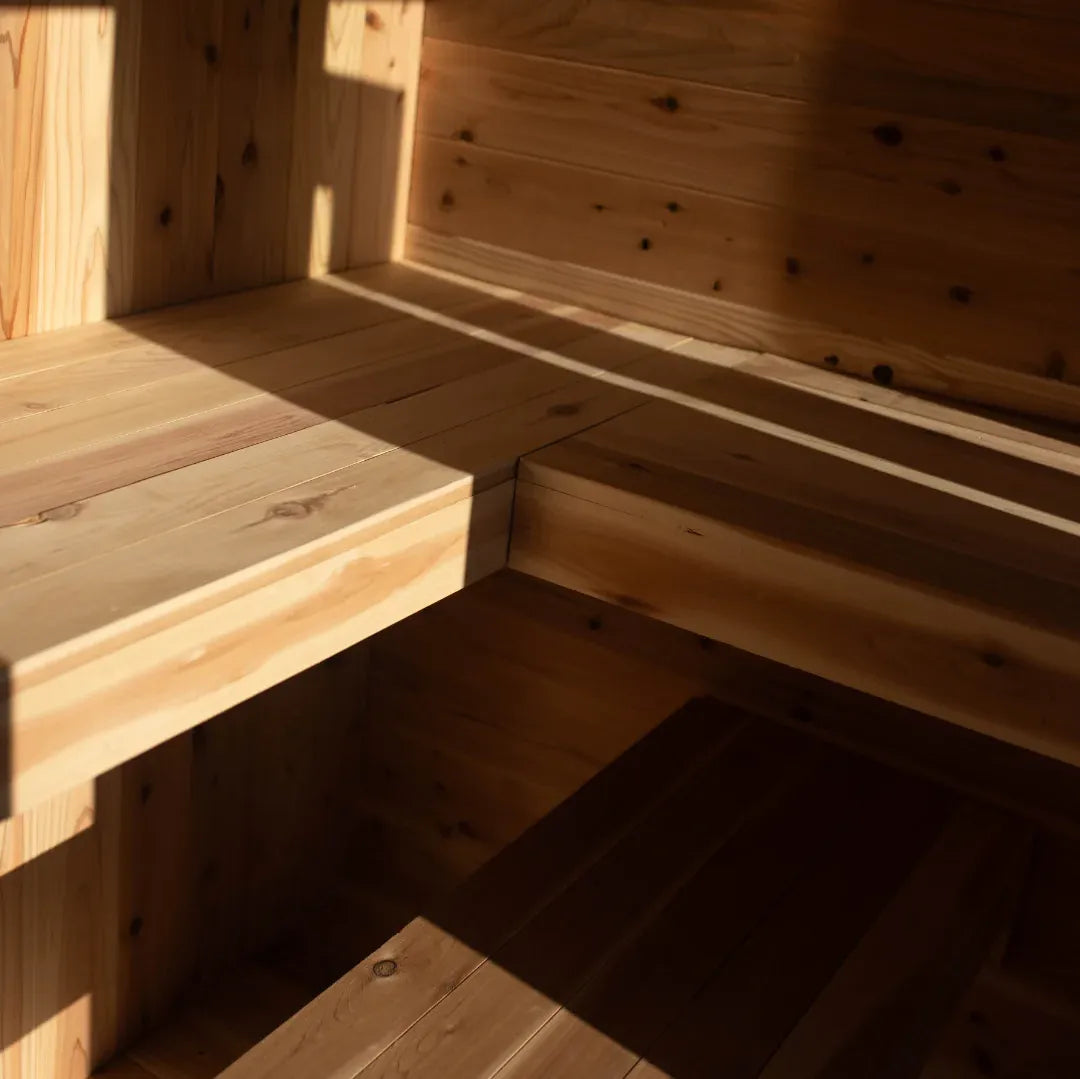 Close-up interior of The Sweat Cabin Deluxe showing the corner where two cedar bench levels meet, with golden sunlight inside.