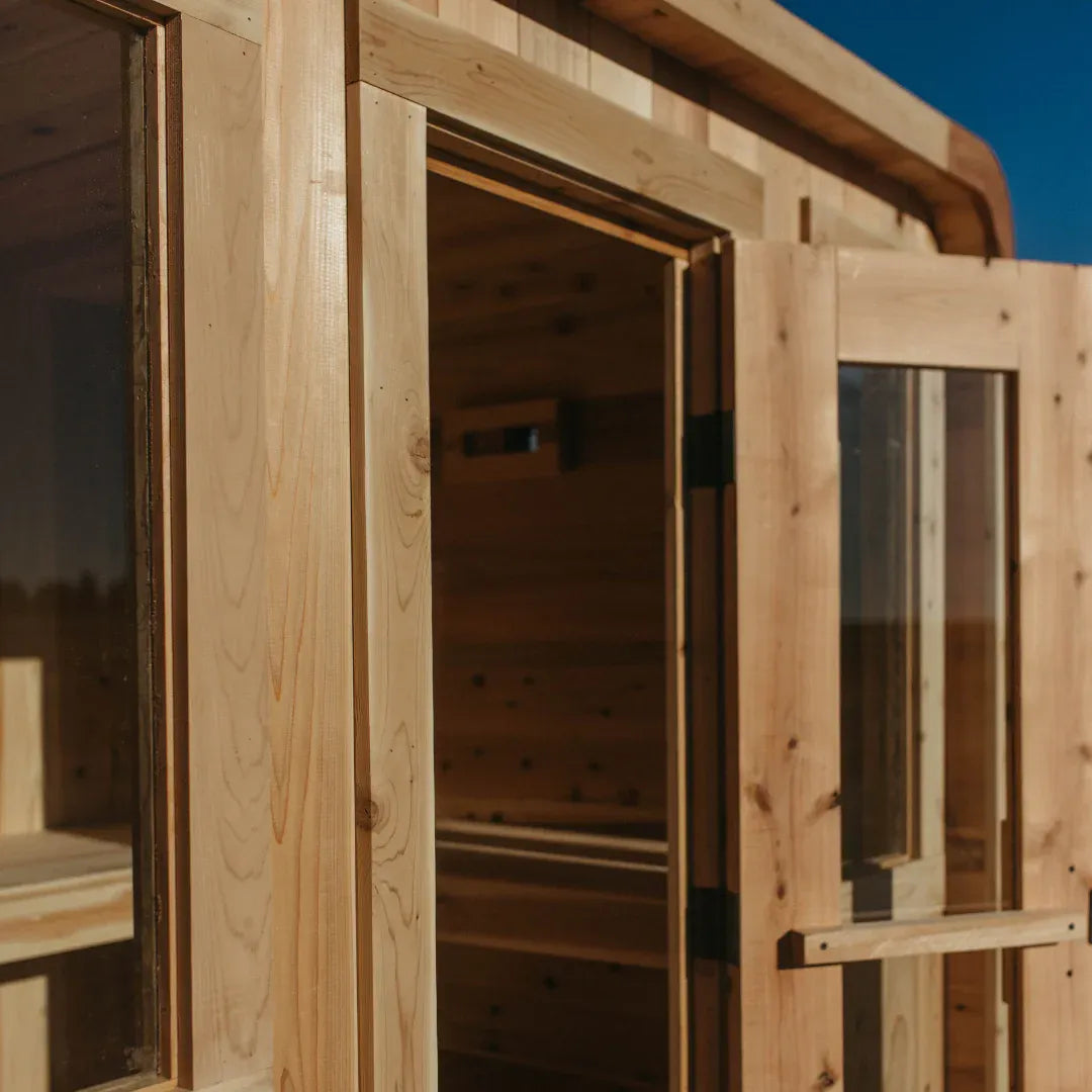 Close-up of The Sweat Cabin Deluxe with the glass door opened showing interior cedar bench, side window, and rear vent.