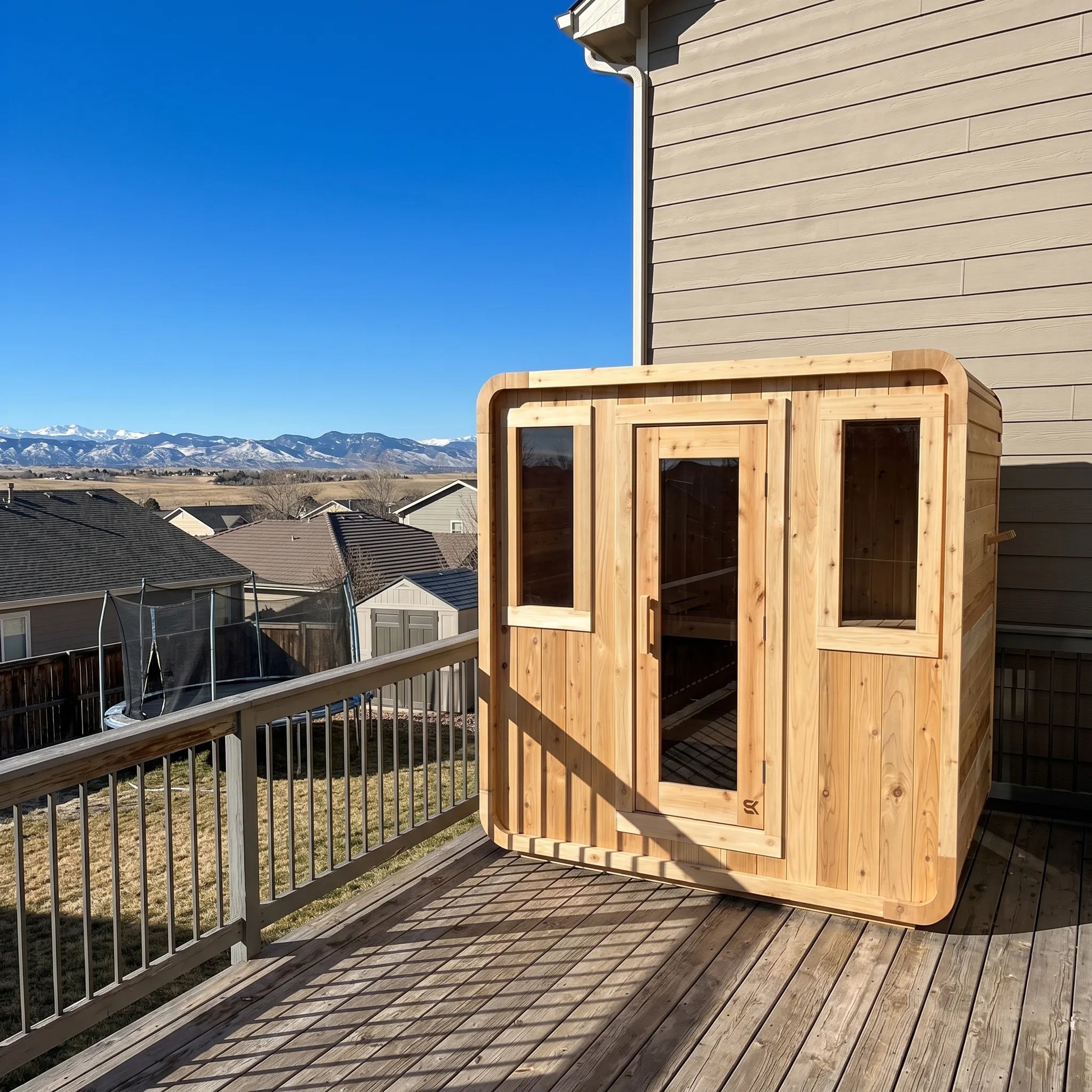 The Sweat Cabin Deluxe cedar 6-person sauna installed on a residential deck overlooking snow-capped mountains and a Colorado neighborhood.