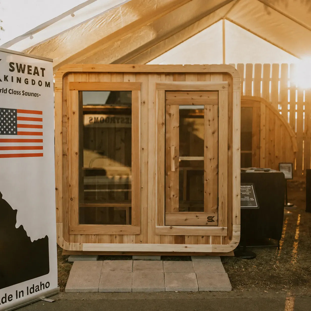 The Sweat Cabin cedar 4-person sauna at a Sweat Kingdom trade show display tent with Made in Idaho banner and American flag.