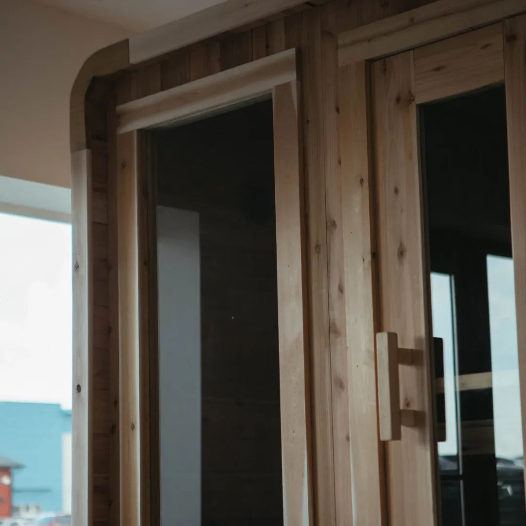 Detail of The Sweat Cabin sauna door handle and large picture window in an indoor showroom installation.