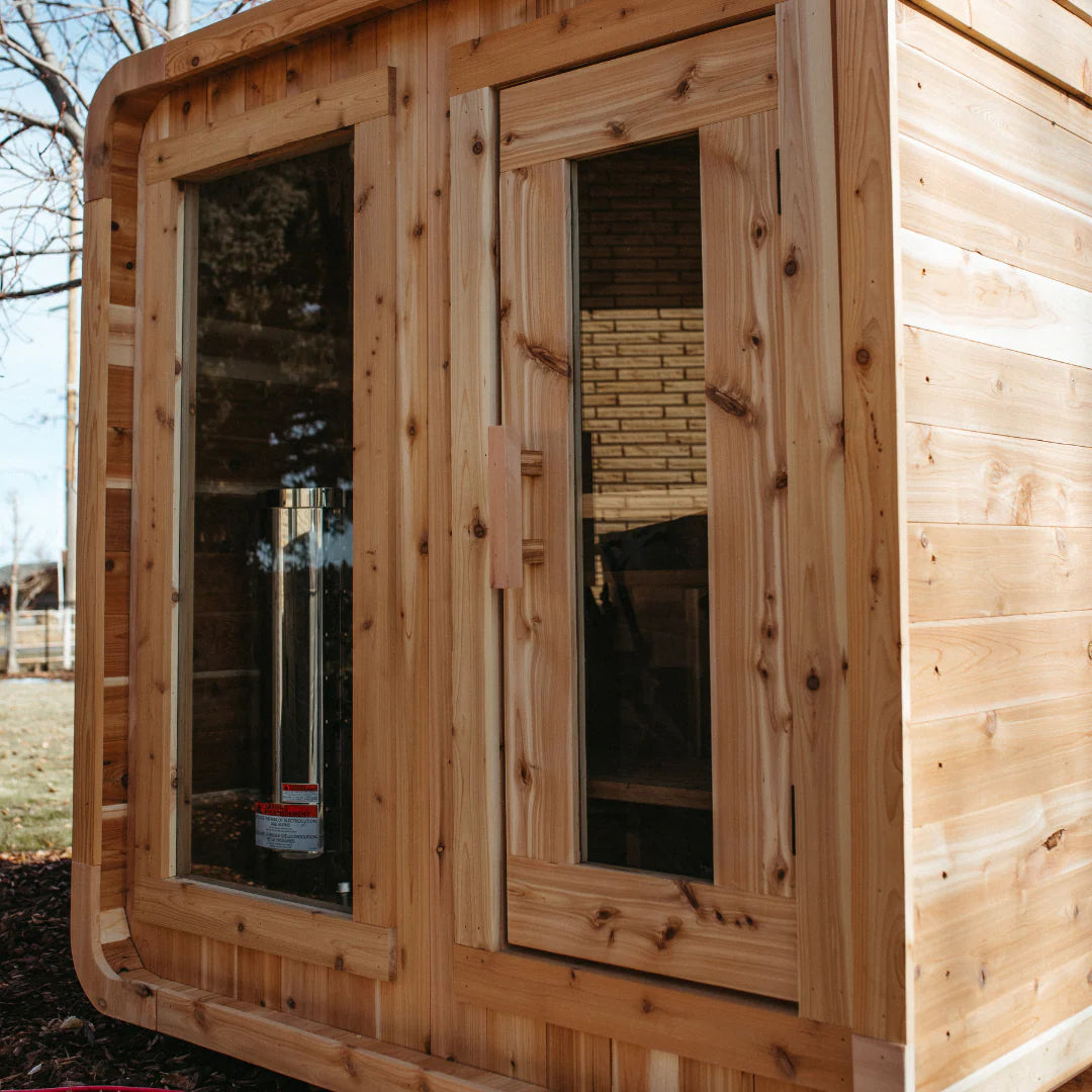 Real customer install of The Sweat Cabin cedar 4-person sauna outdoors with wood-burning chimney visible through the window.
