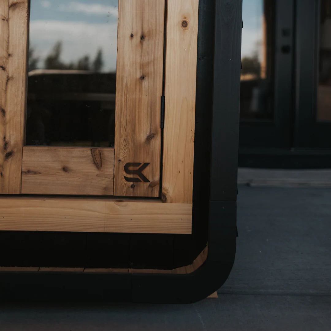 Detail showing contrast between Shou Sugi Ban black charred siding and natural cedar door with Sweat Kingdom SK logo.