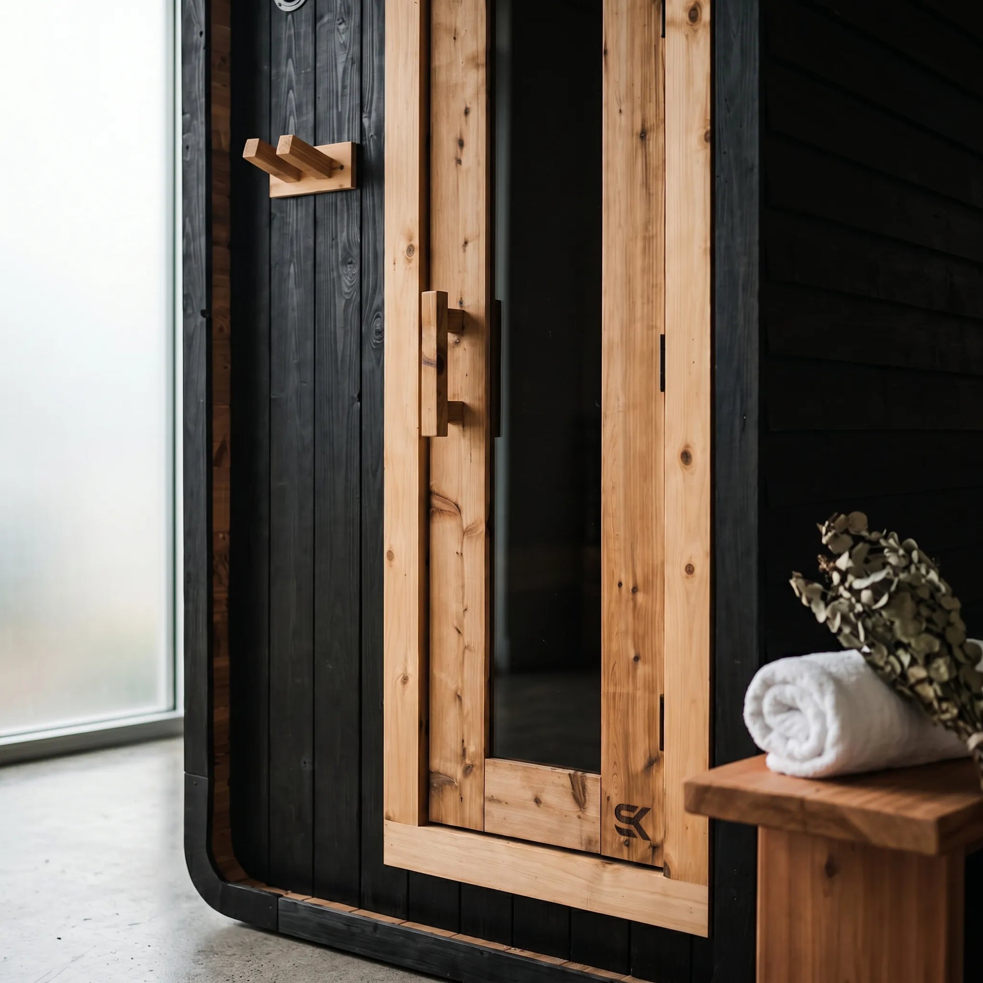 Close-up detail of Shou Sugi Ban charred cedar siding and natural cedar door on The Sweat Pod Black Edition with eucalyptus and towel.