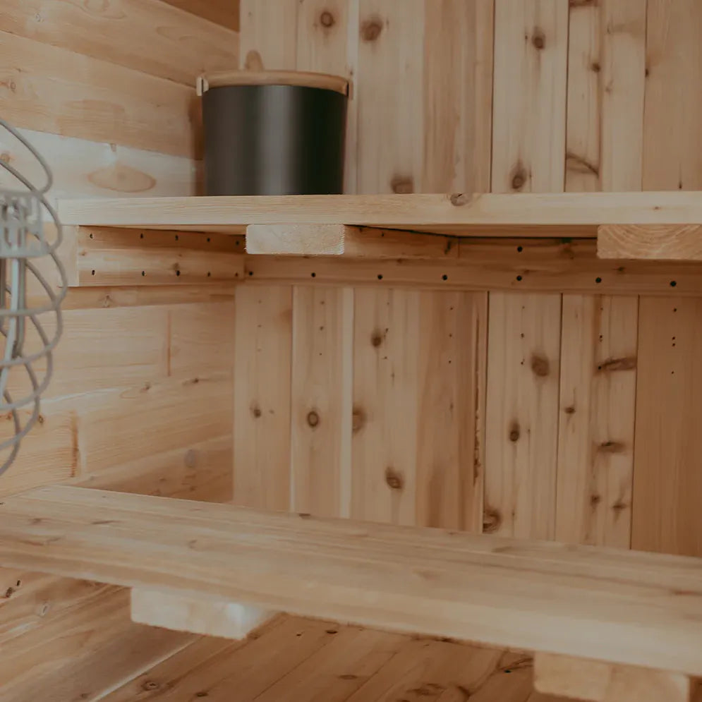 Interior of The Sweat Pod sauna showing two-tier cedar bench layout with KOLO black bucket on the upper bench.