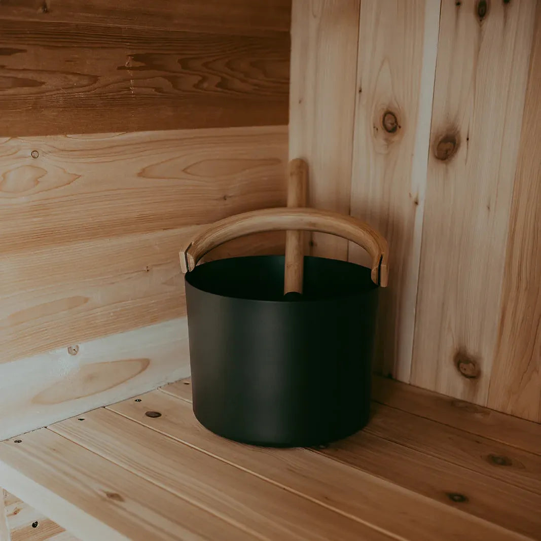 Close-up of the KOLO black sauna bucket with bamboo handle resting on a cedar bench inside The Sweat Pod.