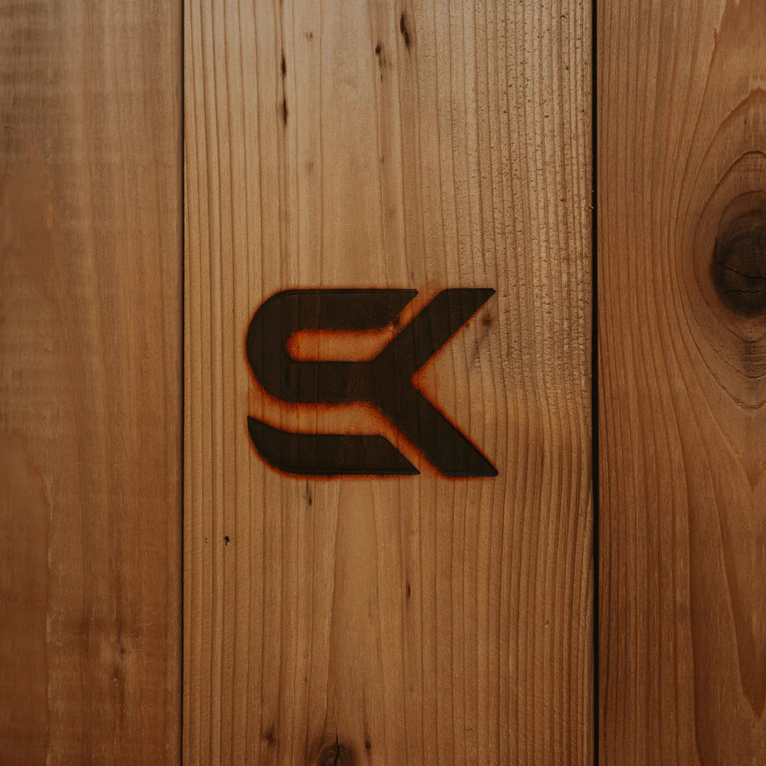 Close-up of the Sweat Kingdom SK logo branded into the cedar siding of The Sweat Pod sauna.