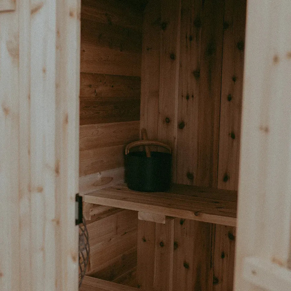Looking inside The Sweat Pod cedar sauna through the doorway showing tiered cedar benches and KOLO black bucket.
