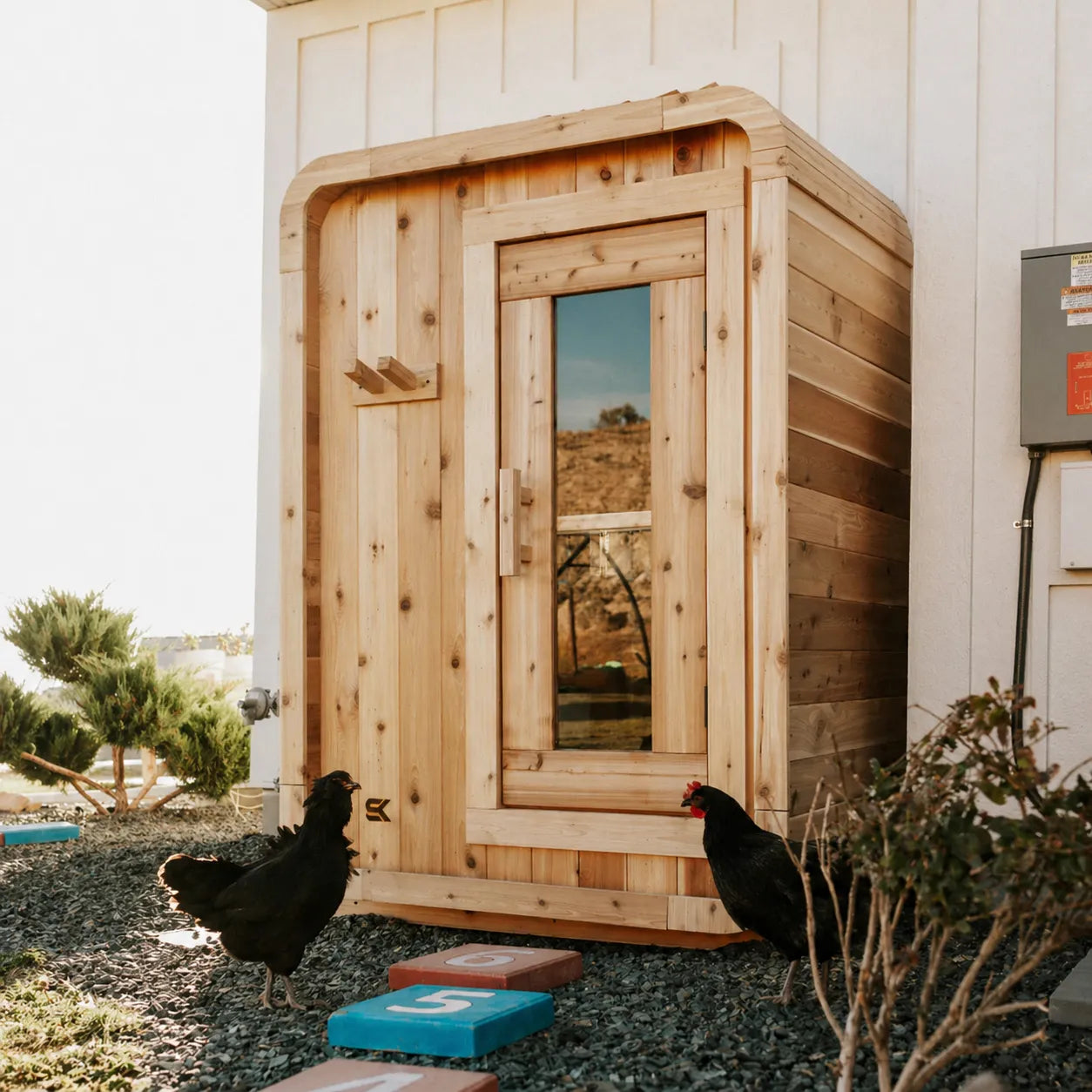 Real customer install of The Sweat Pod cedar sauna outside a desert home with chickens and gravel landscaping.