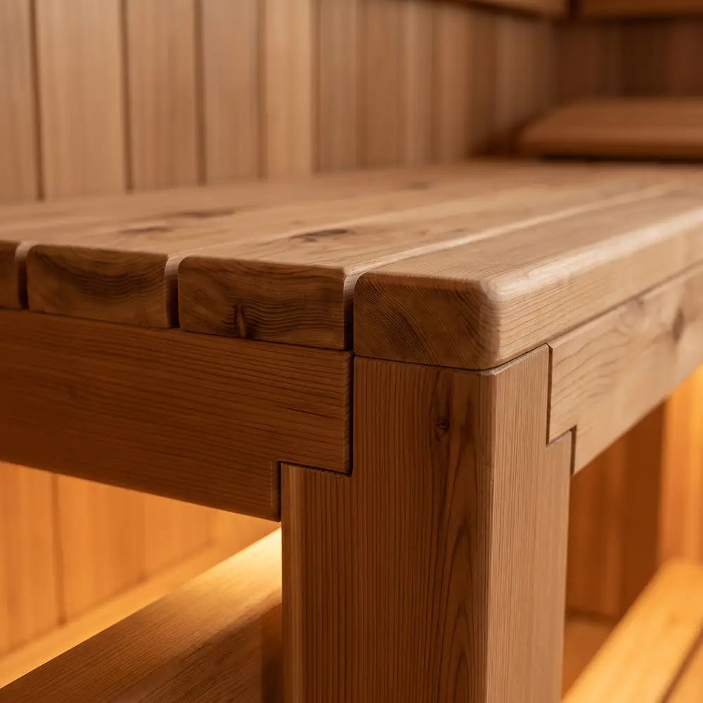 Close-up of a wooden sauna bench corner showing smooth edges, precise joinery, and natural wood grain in a warm, softly lit interior.
