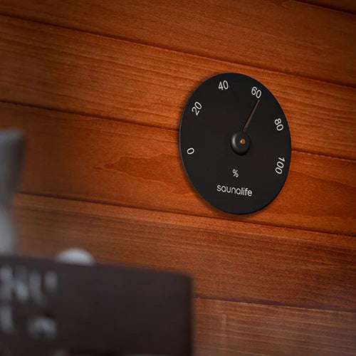 SaunaLife black hygrometer mounted on a wood sauna wall to monitor humidity levels