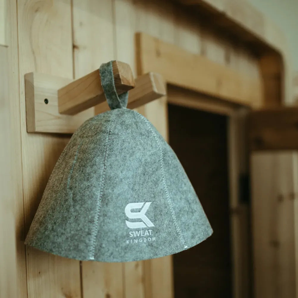 Gray Sweat Kingdom sauna hat hanging from a wooden peg inside a sauna