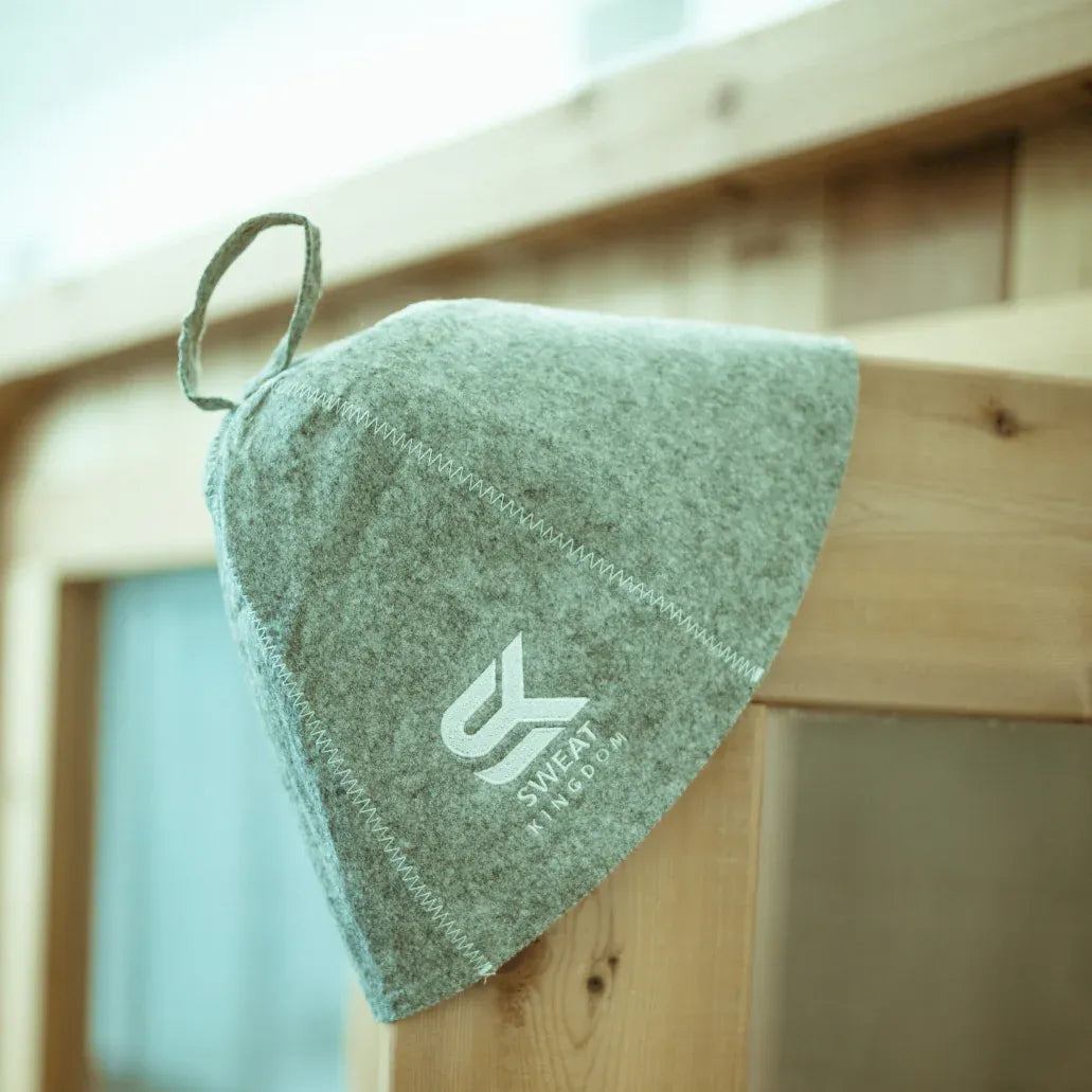 Gray Sweat Kingdom felt sauna hat with hanging loop resting on a wooden sauna bench