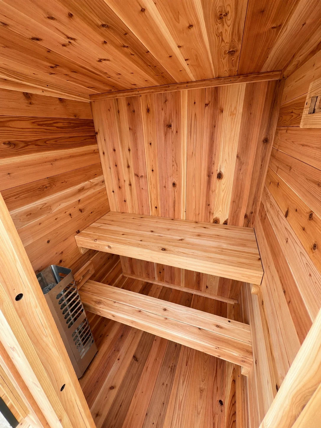 Interior of the Sweat Kingdom Ridge sauna showing the wood bench, lower footrest, and electric heater.