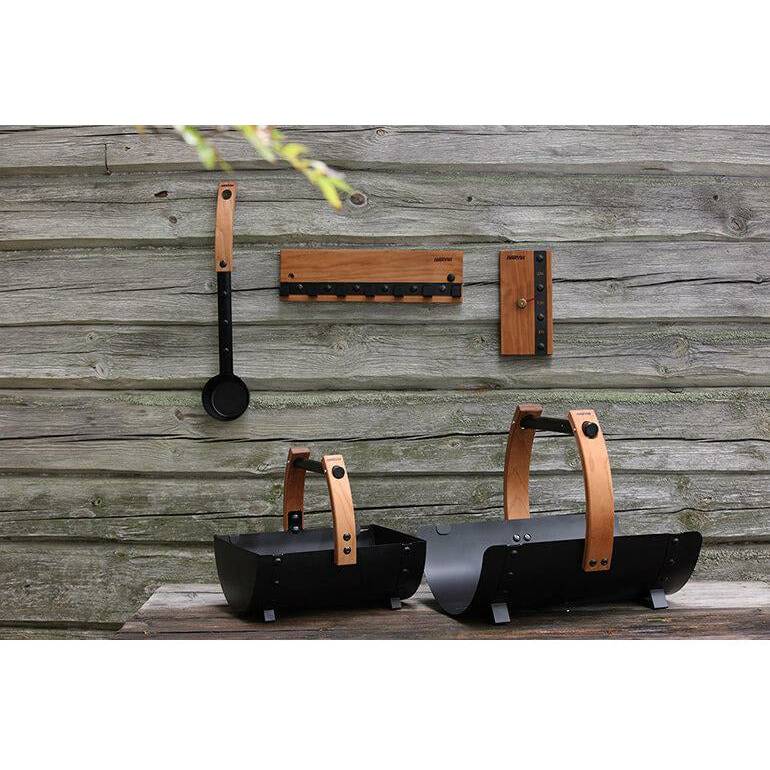 Harvia Legend Ladle SASPO101 Sauna Ladle, displayed hanging on a rustic wood wall alongside an accessory rack and two ember carriers.