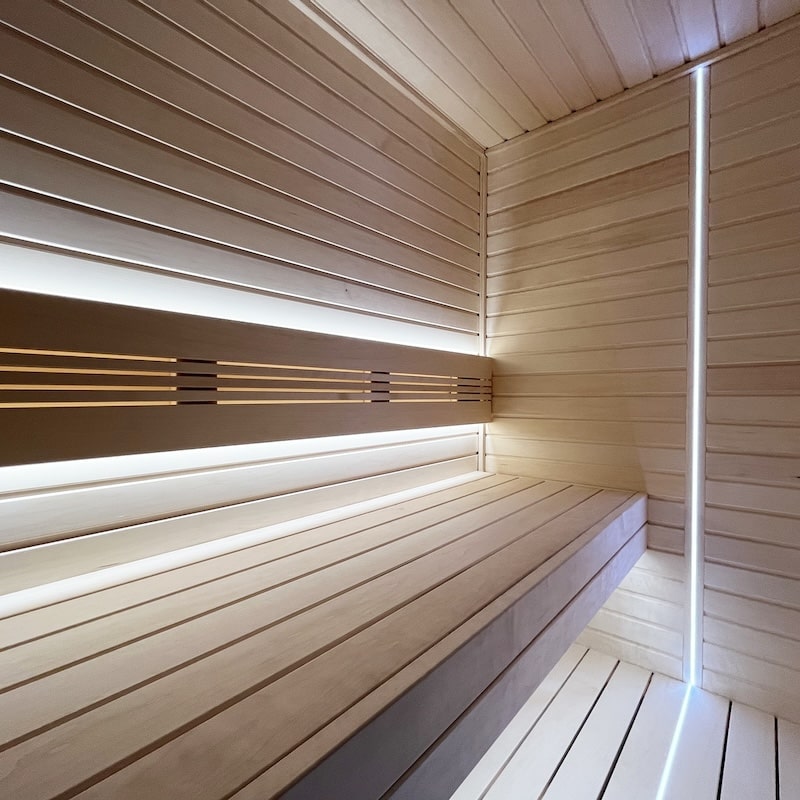Vertical corner and under-bench LED sauna lighting in a light wood sauna interior
